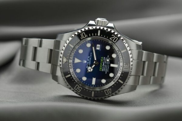 A Rolex Deepsea watch with a blue dial and a stainless steel bracelet laying on its side.